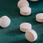 Recovery Supplements - Closeup of spilled similar white round pills placed near plastic container on green surface