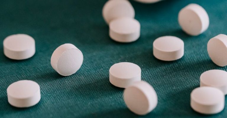 Recovery Supplements - Closeup of spilled similar white round pills placed near plastic container on green surface
