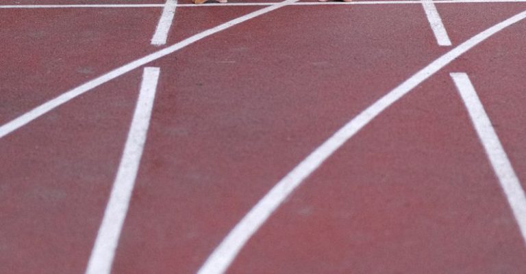 High-Impact Cardio - From above of confident elderly male starting for sprint on racetrack in stadium