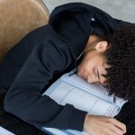 Progressive Overload - High angle of exhausted African American student resting on opened textbook and papers while preparing for exam