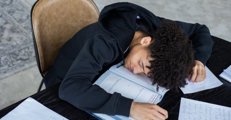 Progressive Overload - High angle of exhausted African American student resting on opened textbook and papers while preparing for exam