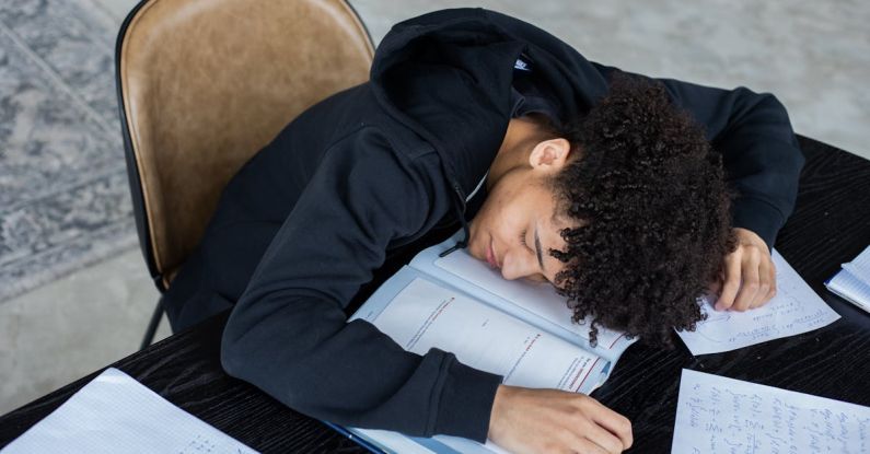 Progressive Overload - High angle of exhausted African American student resting on opened textbook and papers while preparing for exam