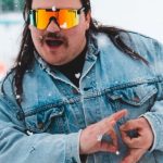 Yin Yoga - Chubby expressive man in denim jacket and skiing glasses showing yin yang mudra with both hands looking at camera in snowfall