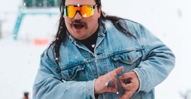 Yin Yoga - Chubby expressive man in denim jacket and skiing glasses showing yin yang mudra with both hands looking at camera in snowfall