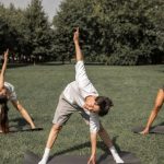 Yoga Practices - Group of diverse friends doing Revolved Wide Legged Forward Bend while exercising yoga on lawn
