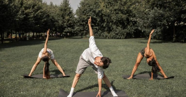 Yoga Practices - Group of diverse friends doing Revolved Wide Legged Forward Bend while exercising yoga on lawn