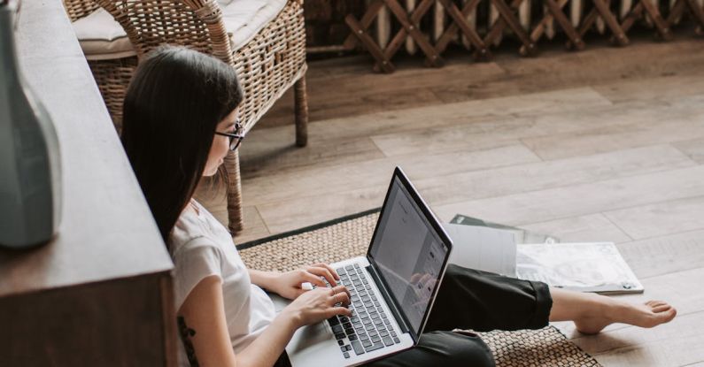 HIIT Program - Young barefoot woman using laptop on floor near books in stylish living room