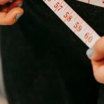 Tracking Calories - From above of crop anonymous plump female using measuring tape around hips in gym