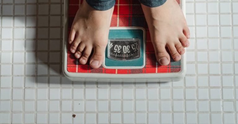 Weight Loss - From above crop anonymous barefoot child in jeans standing on weigh scales on tiled floor of bathroom