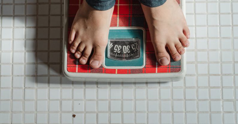 Weight Loss - From above crop anonymous barefoot child in jeans standing on weigh scales on tiled floor of bathroom