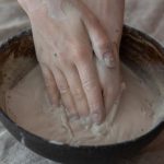 Consistency - From above of crop anonymous craftsperson mixing clay in round shaped bowl in workroom